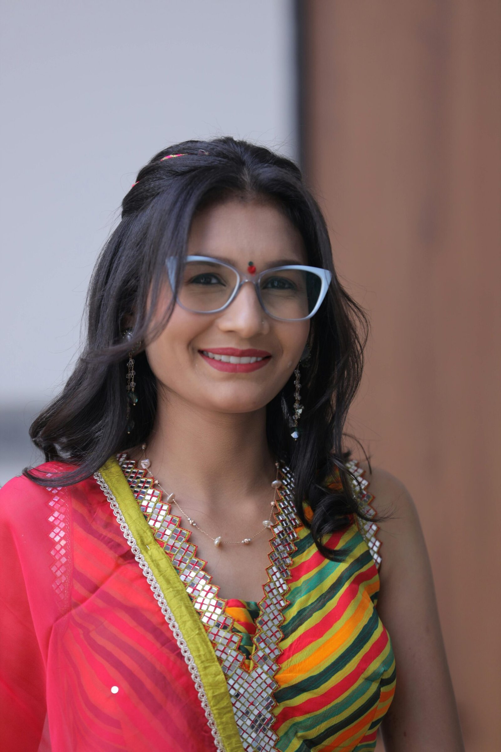 A woman in traditional Indian clothing smiling confidently with colorful patterns.